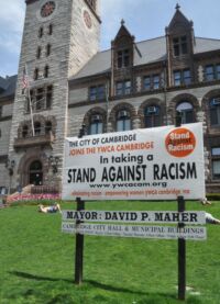 Z billboardu, za nímž vleže na trávníku chytá jarní bronz neznámý tlouštík v trenkách, se dozvídáme, že město Cambridge se oficiálně staví proti rasismu.